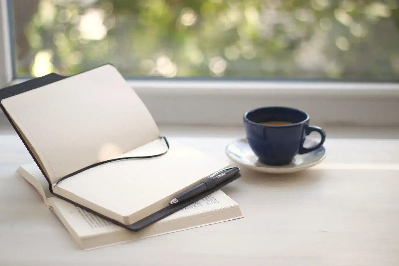 An open notebook and pen beside a cup of coffee on a sunny windowsill, ready for questions about communication, conflict and relationship issues before a first counselling session