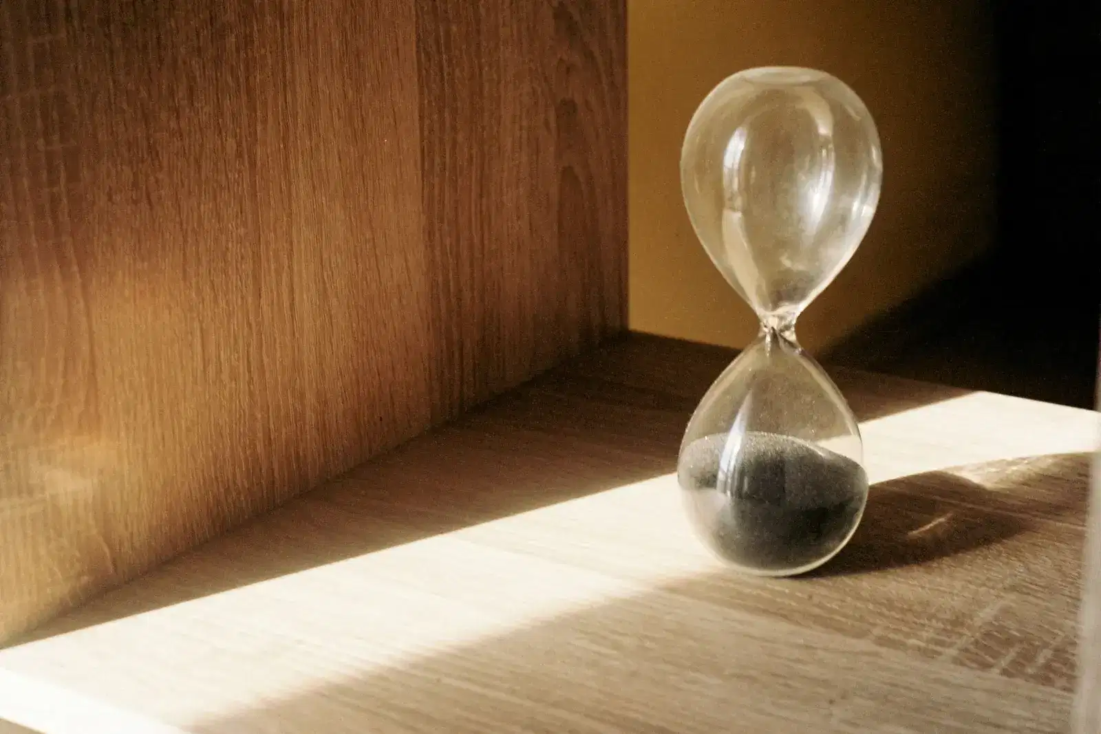 Hourglass with most of its sand run through in warm window light, like the slow exhaustion and stress of parental burnout