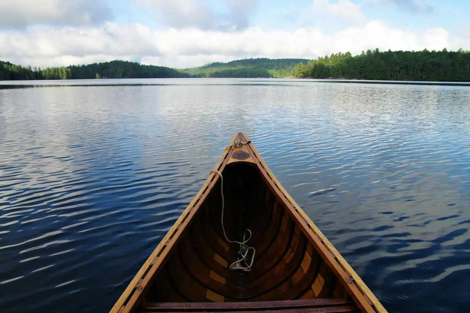 The bow of an empty wooden canoe resting on a calm lake under a bright sky, a quiet reminder that rest matters when you feel unable to relax.