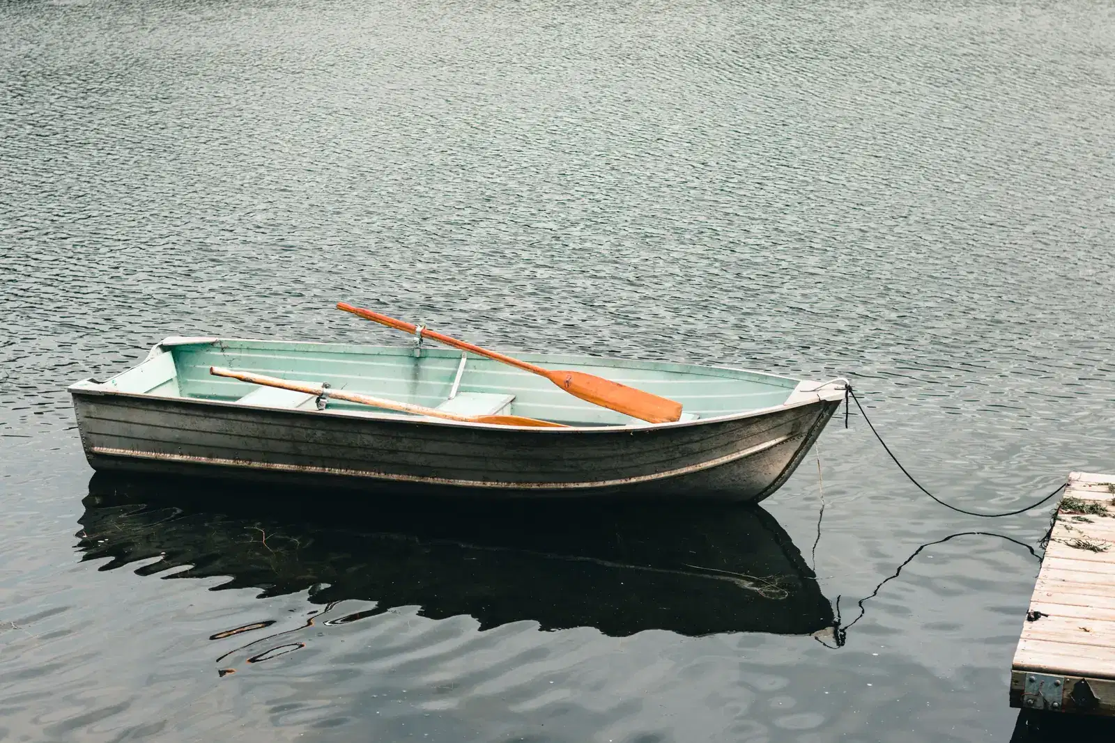 A small rowboat tied safely to a wooden dock on calm water, a steady place to rest while grieving