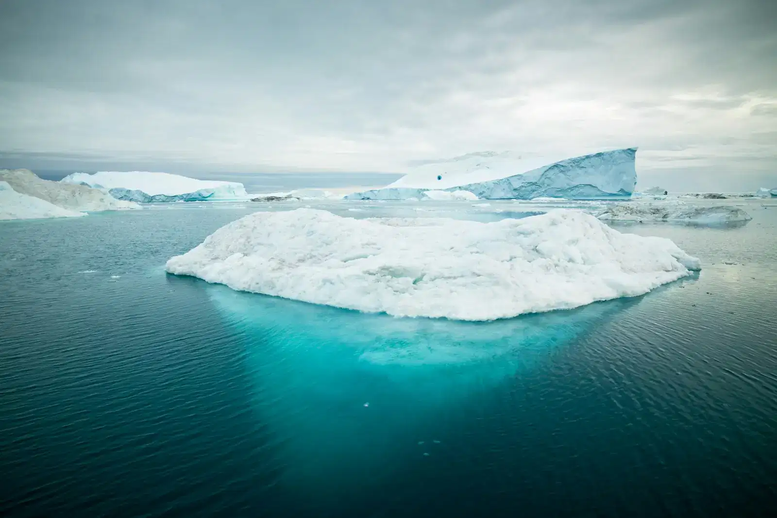 An iceberg on calm teal water with most of its mass hidden below the surface, an image of a quiet panic attack: calm on the outside, with intense fear, a racing heart and physical symptoms hidden underneath.