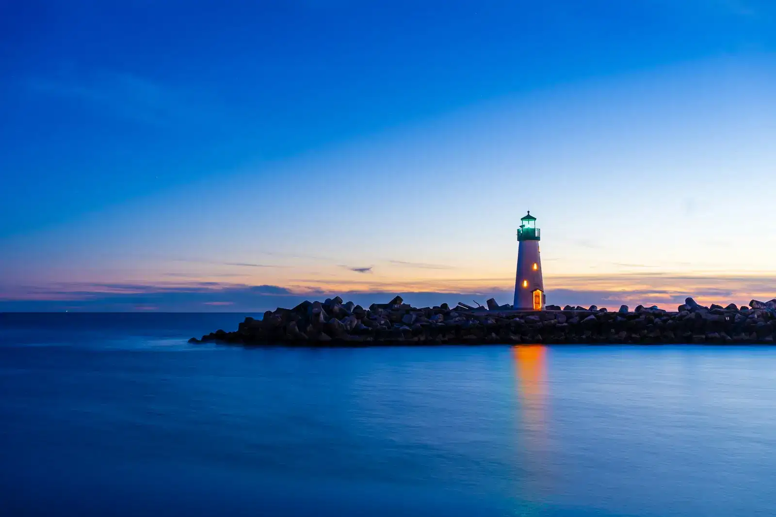 Lighthouse on a stone breakwater at blue hour, a steady guide for anyone working to stop gambling for good and rebuild their savings.