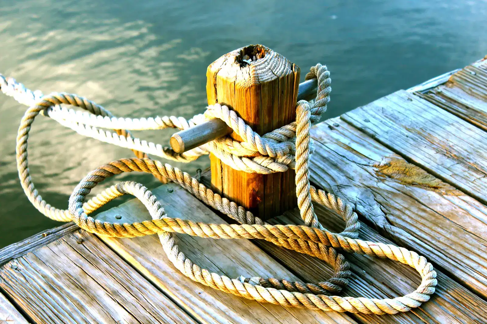 A thick rope wrapped around a wooden bollard on a sunlit dock above calm water, an image of grounding and staying anchored in the present moment, a steady calm when panic attacks rise, with slow breathing and feet on the floor.