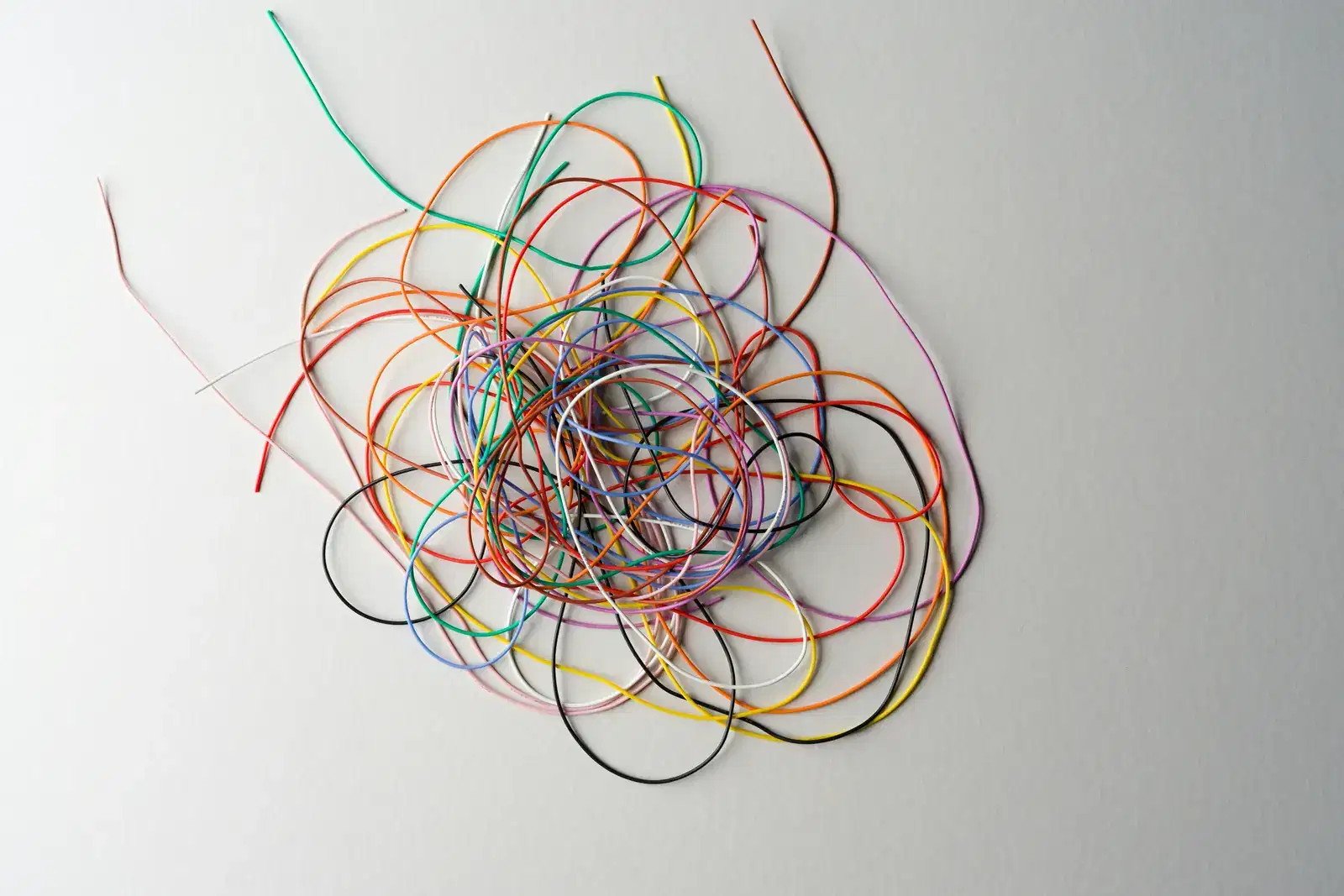 A tangled knot of coloured wire on a pale surface, like an overthinking spiral of thoughts, worry and what if questions, showing what causes overthinking and why you overthink.
