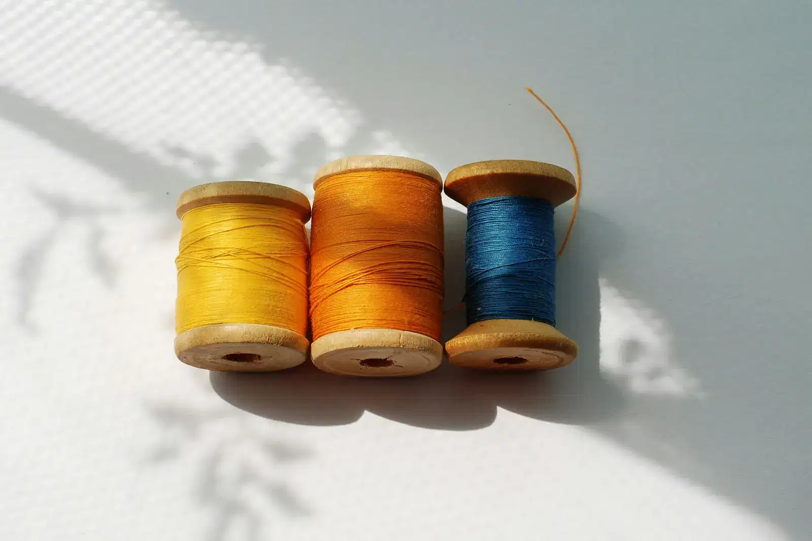 Three spools of neatly wound thread in yellow, orange and blue on a sunlit table, a calm picture of how to overcome overthinking and stop overthinking everything, with thoughts, worry and the mind settled into calmer patterns, and less stress and anxiety.