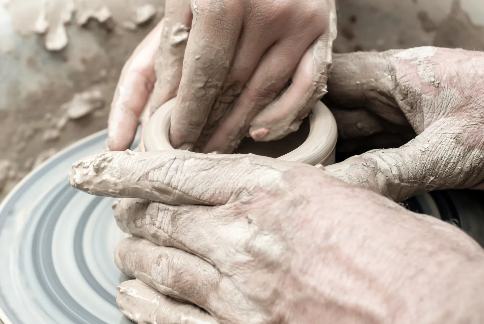 Two people's hands shaping a clay pot together on a pottery wheel, an image for couples therapy