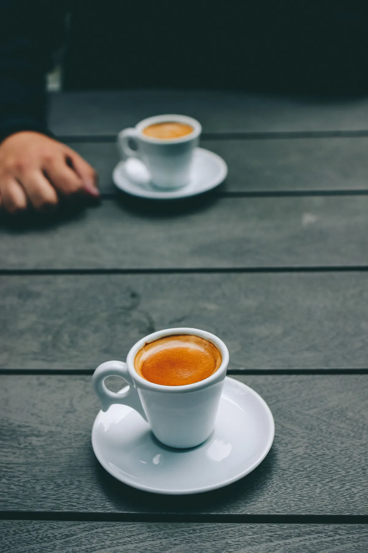 Two espresso cups set apart at opposite ends of a long wooden table, an image for couples therapy after infidelity