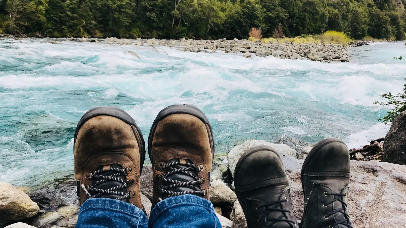 Two pairs of hiking boots side by side on the rocks above a rushing river, an image for marriage preparation
