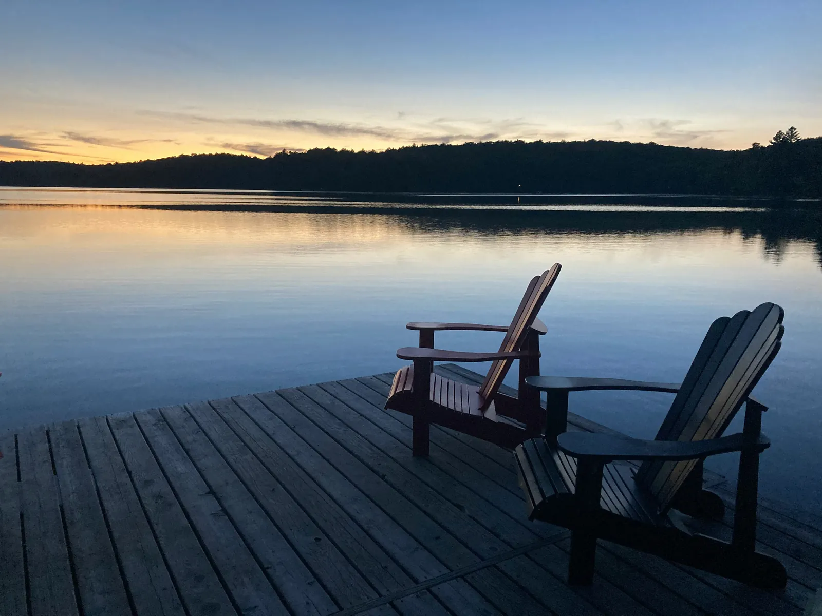 Two wooden Adirondack chairs on a dock overlooking a still lake at dusk, an image for marriage therapy