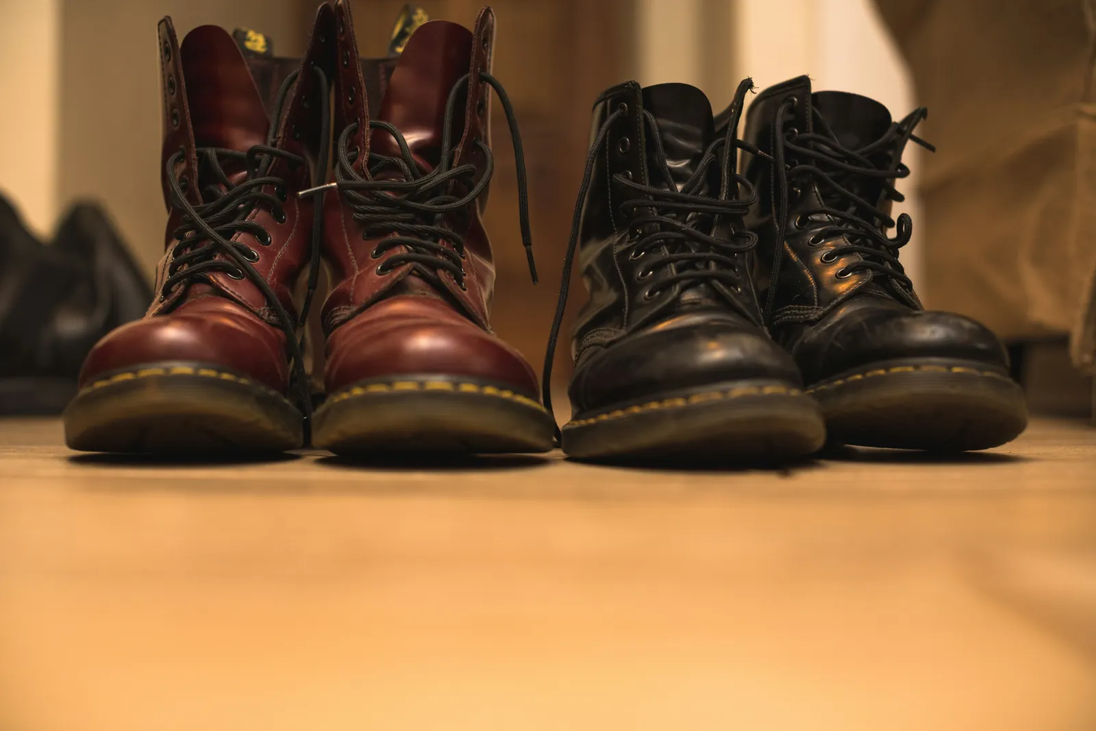 Two pairs of worn leather boots standing side by side in warm light, a picture of sharing a home but drifting apart