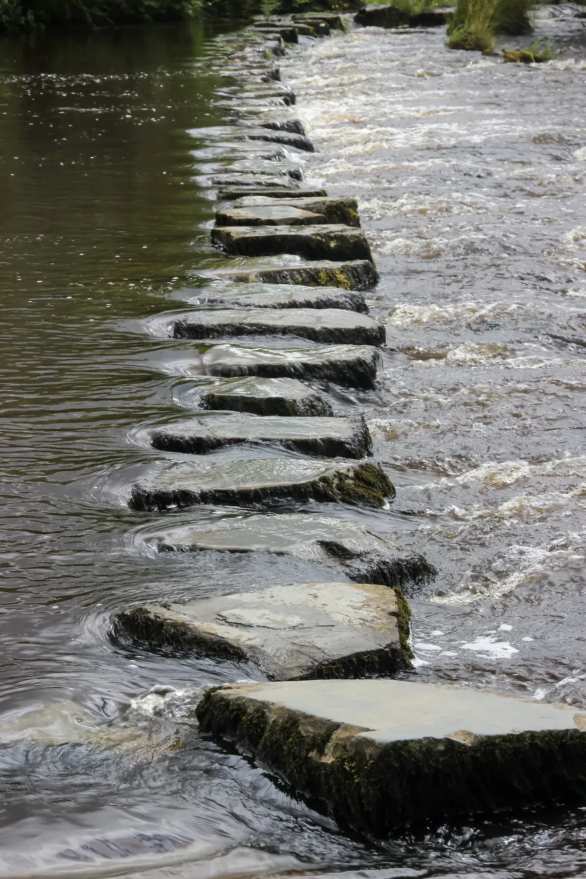 Flat stepping stones leading across a flowing river, an image for rebuilding trust in infidelity therapy