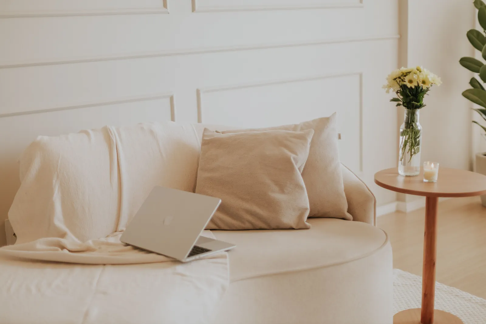 An open laptop resting on a cream sofa with soft cushions and fresh flowers nearby, an image for virtual couples therapy